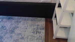 A neatly made bed with white bedding, a wooden headboard, and a white bedside table with a glass container.
