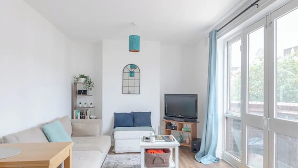A modern living room with a sofa, a coffee table, a TV, and a large window with curtains.