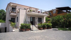 A two-story building with a central balcony, potted plants, and a cobblestone driveway. - Villa with pool (Pompei)