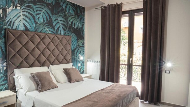 A bedroom with a large bed, a tufted headboard, a nightstand, and a view of the outside through a window with curtains. - Villa with pool (Pompei)