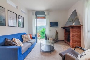 Un salon avec un canapé bleu, une table basse en verre, un téléviseur fixé au mur et une cheminée en briques.