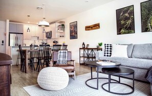 Een moderne keuken met roestvrijstalen apparatuur, een eethoek met een tafel en stoelen, een grijze bank en een salontafel.