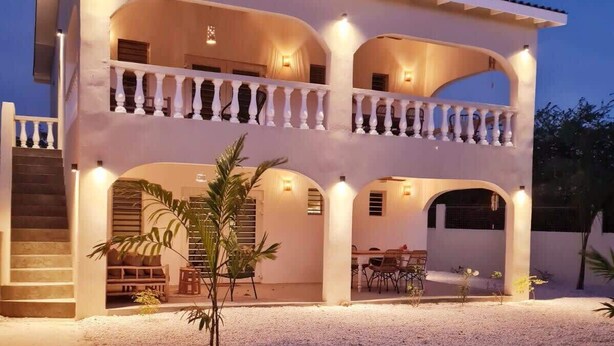 A two-story building with a covered patio area, outdoor seating, and a small garden. - 12B Flamingo by Bonaire Paradise (Kralendijk)