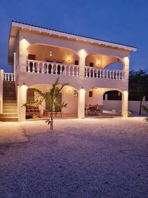 A two-story building with a covered patio area, outdoor seating, and a small garden. - 12B Flamingo by Bonaire Paradise (Kralendijk)