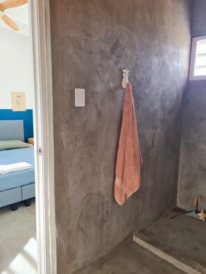 A room with a concrete wall, a bed with a blue mattress, and a towel hanging on a hook. - 12B Flamingo by Bonaire Paradise (Kralendijk)