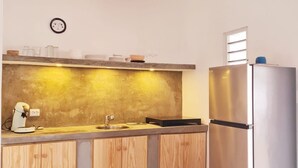 A modern kitchen with wooden cabinets, a stainless steel refrigerator, a hanging pendant light, and a small clock on the wall. - 12B Flamingo by Bonaire Paradise (Kralendijk)