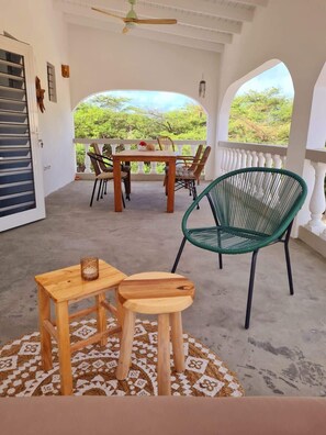 A covered outdoor seating area with a table and chairs, a green chair, and a patterned rug. - 12B Flamingo by Bonaire Paradise (Kralendijk)