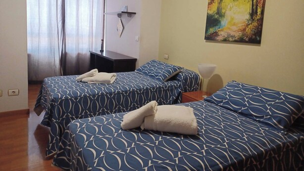 A hotel room with two beds, a painting on the wall, and a desk with a lamp. - Apartamento Vigo Playa-ciudad II (Vigo)