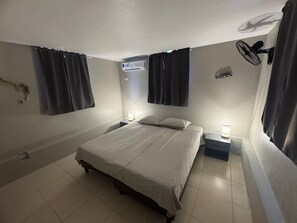 Une chambre à coucher comprenant un lit, deux tables de chevet avec des lampes, un climatiseur fixé au mur et un ventilateur de plafond.