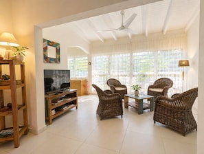 Un salón con televisor, muebles de mimbre y ventanas amplias.