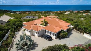 A large house with a red-tiled roof, surrounded by greenery and a view of the ocean. - Crown Terrace 18 by Bookaparadise (Kralendijk)