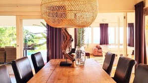 A dining area with a wooden table and black chairs, a woven light fixture, and a vase with a plant. - Crown Terrace 18 by Bookaparadise (Kralendijk)