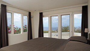 A bedroom with a large bed, a view of the sea, and a balcony with flowers. - Crown Terrace 18 by Bookaparadise (Kralendijk)