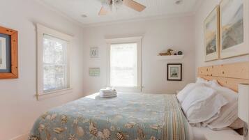 A bedroom with a bed, a ceiling fan, and two windows with blinds.