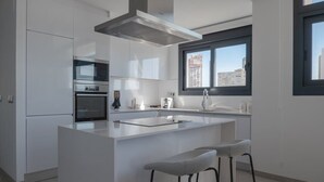 Een moderne keuken met witte kasten, een roestvrijstalen afzuigkap, een ingebouwde oven, een groot kookeiland met een spoelbak en een raam met uitzicht over de stad.