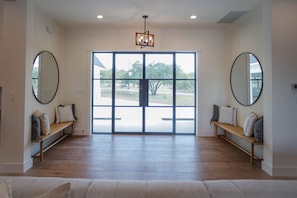 A spacious entryway with a large glass door, two benches with cushions, and a chandelier.