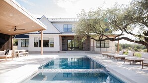 Ein modernes Haus mit Swimmingpool, Sitzgelegenheiten im Freien und einem großen Baum.
