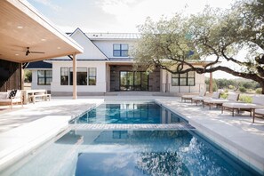 A modern house with a swimming pool, outdoor seating, and a large tree.