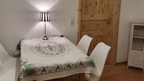 A dining area with a table covered by a patterned tablecloth, white chairs, a lamp, and a wooden door. - Vacation apartment Bergblick (Königstein)