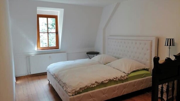 A bedroom with a large bed, a window, a radiator, a small table, and a lamp. - Vacation apartment Bergblick (Königstein)