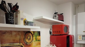 A kitchen with a red stove, microwave, and oven. There are utensils on a shelf and a kettle on the counter. - Vacation apartment Bergblick (Königstein)
