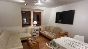 A compact living space with a sofa, a small bed, a wooden coffee table, and a TV mounted on the wall. - Vacation apartment Bergblick (Königstein)