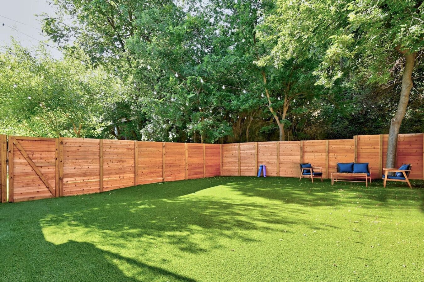 A fenced backyard with artificial grass, a wooden deck, and outdoor furniture.