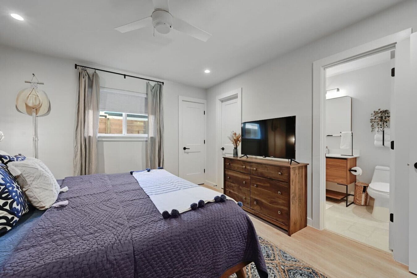 Un dormitorio con una cama, un aparador, un televisor y un baño visible a través de una puerta abierta.