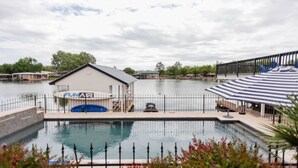 A swimming pool with a fenced area, a building labeled 'FUNAR', and a covered seating area with umbrellas.