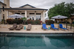 A poolside area with lounge chairs and umbrellas, a covered patio, and a stone building in the background.
