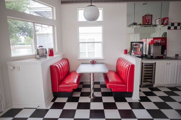 A kitchen with a checkered floor, red booths, a white table, and a window with a view of trees.