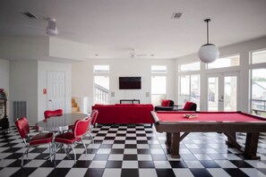 A room with a pool table, red chairs, a red sofa, and a billiards set.
