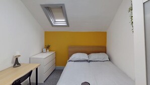 A small, compact bedroom with a single bed, a bedside table, a desk, and a window with a skylight. - City Centre-university Home From Home (Sunderland)