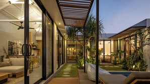 Una casa moderna con un área de estar con paredes de vidrio, una terraza de madera y un pequeño jardín con piscina.