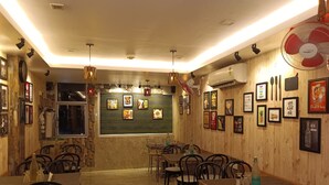 A restaurant with wooden walls, multiple tables and chairs, and various framed pictures on the walls. - Hotel Vedant (Port Blair)