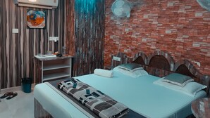 A modern bedroom with a brick wall, a ceiling fan, a mounted air conditioner, and a bed with a patterned bedspread. - Hotel Vedant (Port Blair)