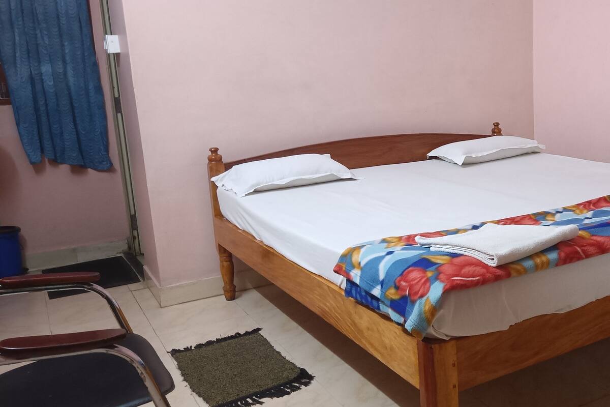 A single bed with a wooden frame, white bedding, and a colorful floral blanket.