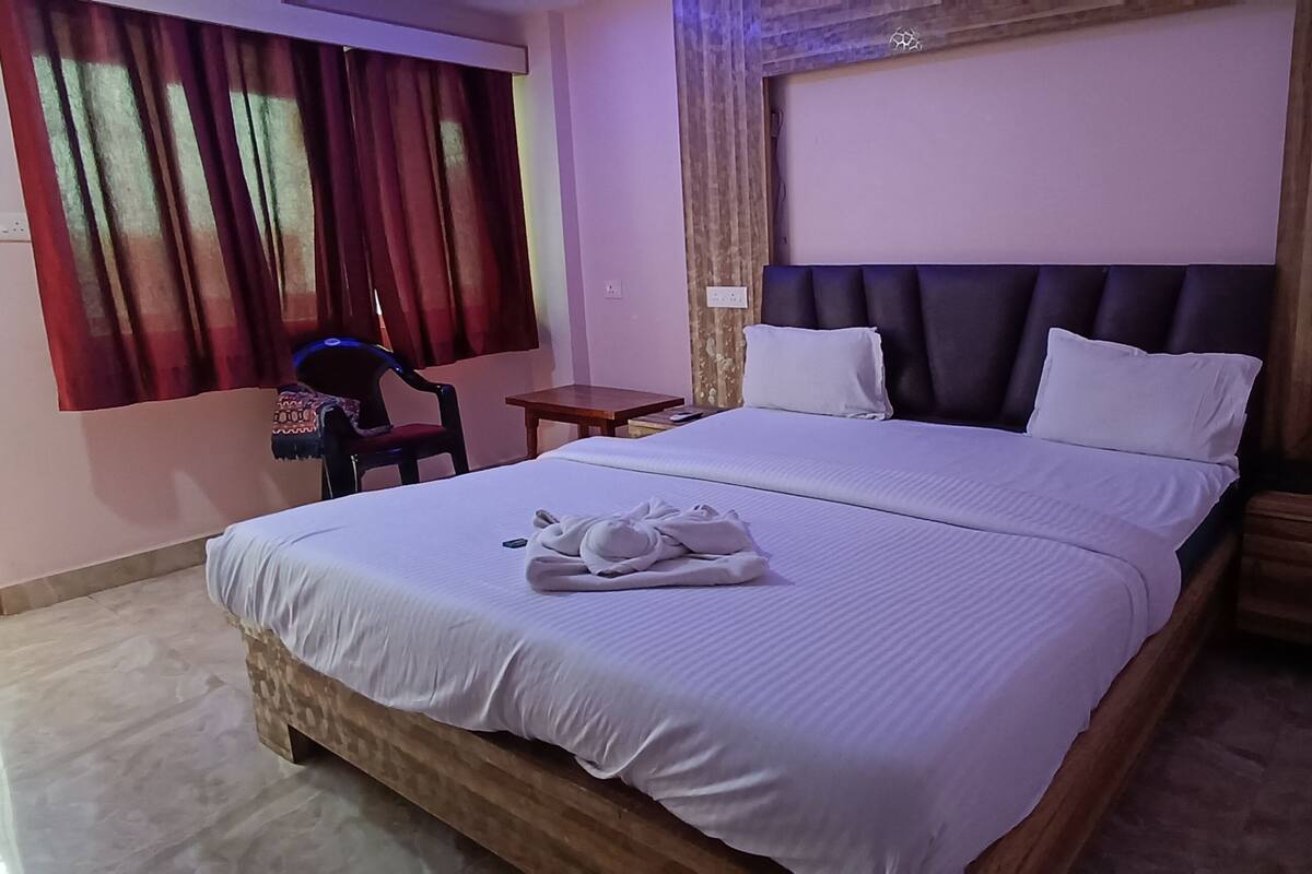 A hotel room with a large bed, a small table, a chair, and a window with curtains.