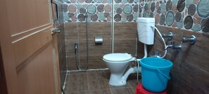 Ein Badezimmer mit Toilette, Dusche und einem blauen Eimer.
