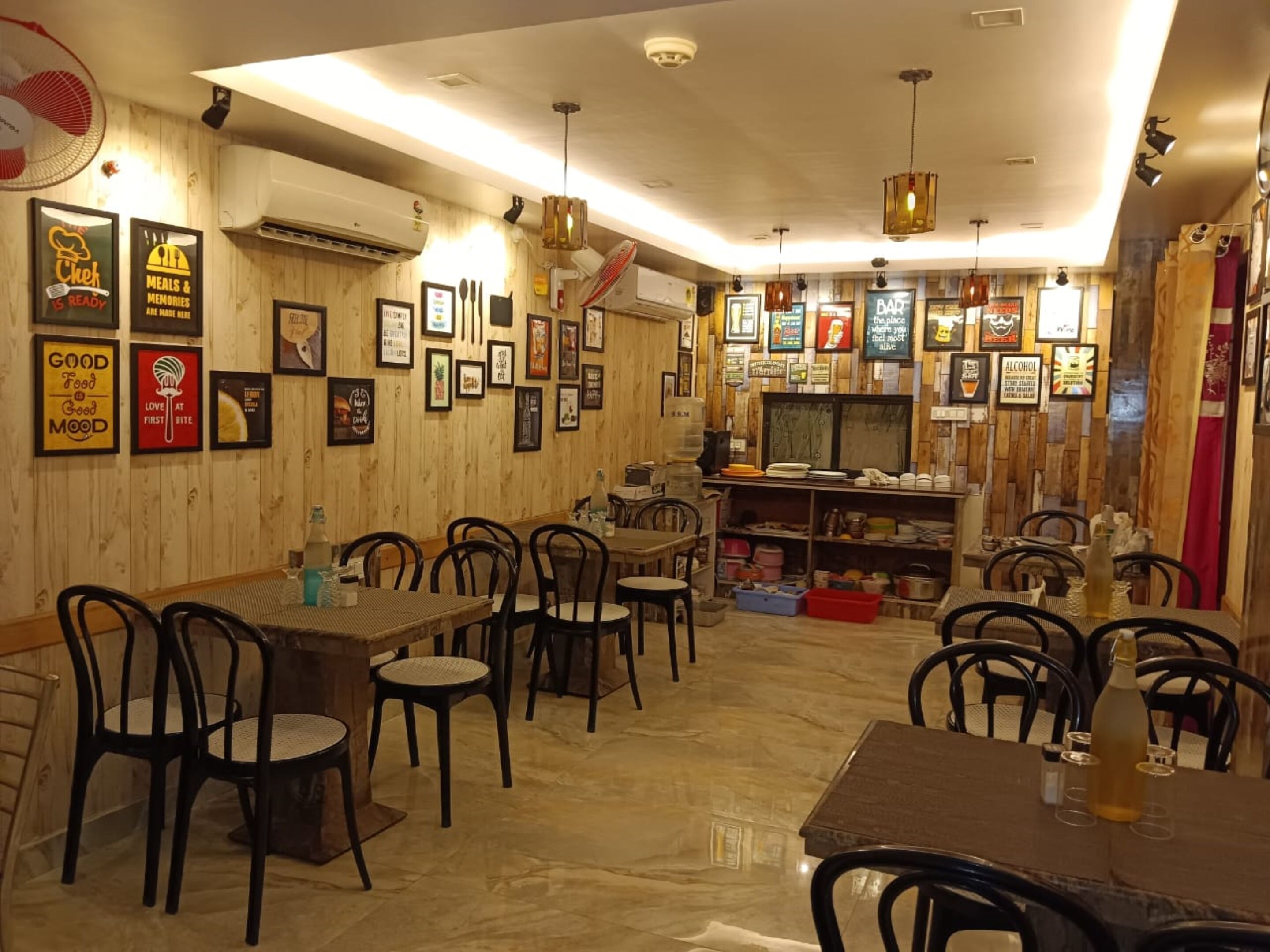 Un restaurante con paredes de madera, cuadros enmarcados y una zona de bar. Mesas y sillas dispuestas para comer.