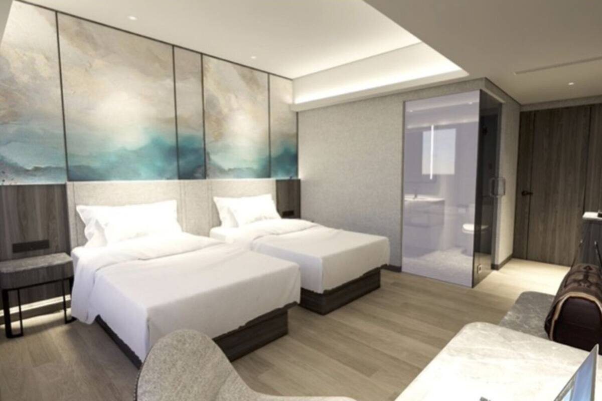 Ein modernes Hotelzimmer mit zwei Betten, einer Sitzecke, einem großen Kunstwerk an der Wand und einem durch eine Glastür einsehbaren Badezimmer.