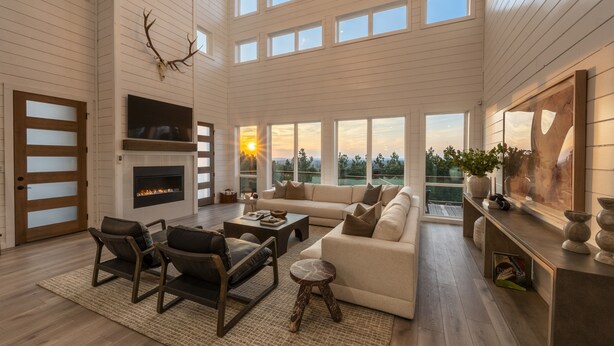 A spacious living room with a fireplace, large windows, and a high ceiling.