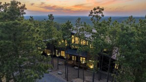 A modern cabin with a view of the ocean at sunset, surrounded by pine trees.