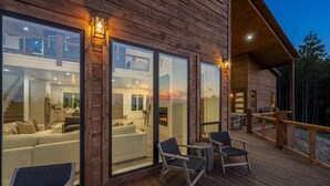 A wooden cabin with large sliding glass doors, a deck with outdoor seating, and a visible interior with a fireplace.