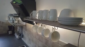 Une cuisine avec une étagère où sont rangées des tasses et des bols blancs, une machine à café et des ustensiles de cuisine.