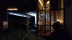 Une entrée de garage faiblement éclairée, avec une voiture garée à l’intérieur, un panneau portant le numéro « 82 » et un escalier menant à un intérieur éclairé.