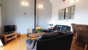 Una sala de estar con un sofá de cuero negro, una mesa de centro de madera, un televisor sobre un mueble de madera, una chimenea y un espejo en la pared.