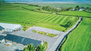 Vista aérea de una propiedad rural con campos verdes, una zona pavimentada con un edificio y una carretera.