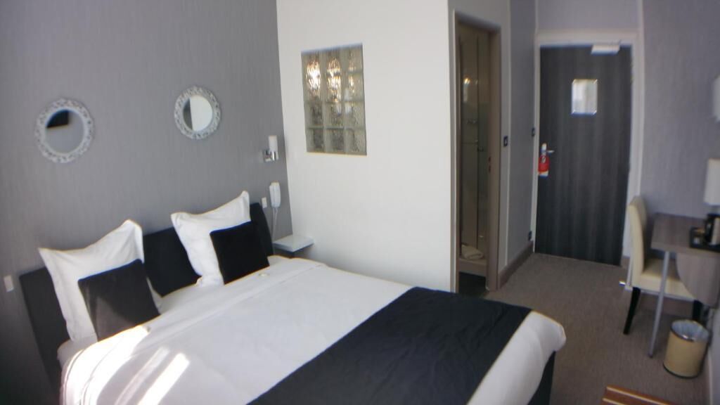 A hotel room with a large bed, a desk, a chair, and a door.