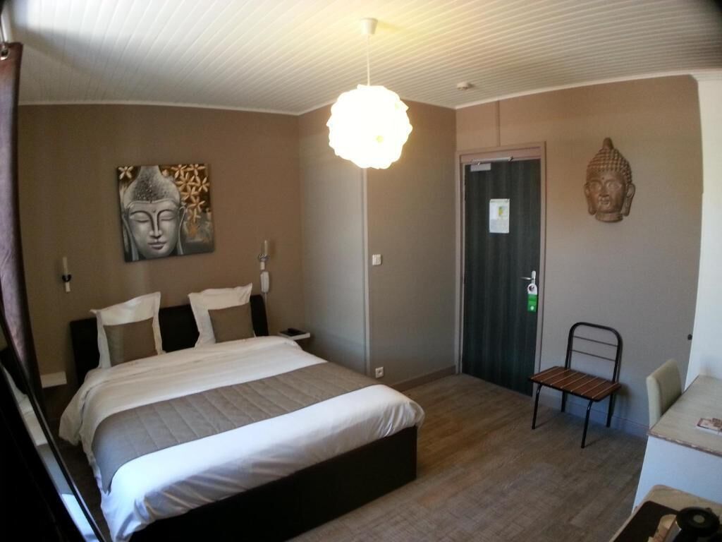 A bedroom with a bed, a chair, a Buddha statue, and a wall with a Buddha painting.